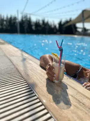 a person laying next to a swimming pool with a drink at Burgaz İzer Hotel in Lüleburgaz