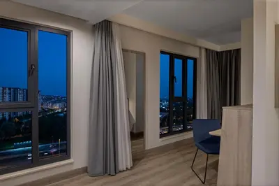 a room with large windows with a blue chair and a desk at Hampton By Hilton Istanbul Merter in Istanbul
