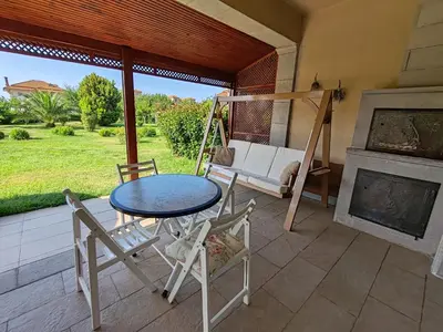 a patio with a table and chairs and a swing at Garden Floor Flat in a Beachfront Complex with a Pool in Gümüşyaka