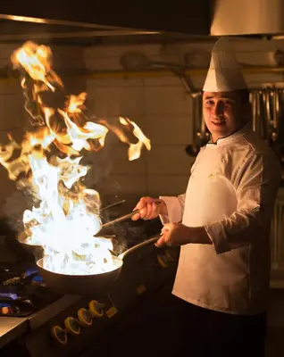 a chef cooking in a pan with fire in it at Metropolitan Hotels Taksim in Istanbul