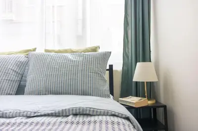a bed with blue and white sheets and a table with a lamp at Pretty Corner Flat with Abundant Light in Kadikoy in Istanbul