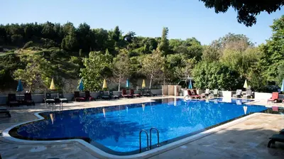 a large swimming pool with chairs and a mountain in the background at Fener Motel in Sile