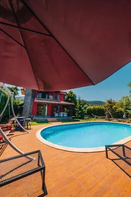 a swimming pool with a red umbrella on a wooden deck at Sapancada ısıtmalı havuzlu villa in Sapanca