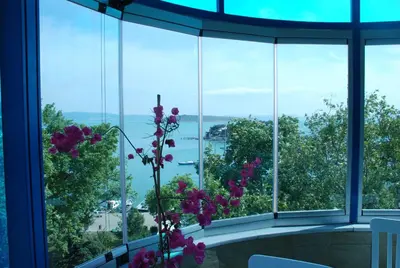a vase with purple flowers in a room with windows at Mavi Inci Park Otel in Erdek