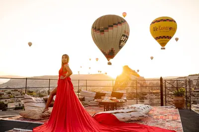 a woman in a red dress standing on a balcony with hot air balloons at Zenith Göreme in Istanbul