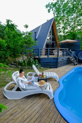 a man sitting on a lounge chair next to a pool at sapancakelebekvadibungalov in Sapanca