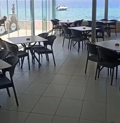 an empty restaurant with tables and chairs and the ocean at Kum Motel in Marmara