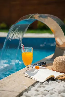 a glass of orange juice sitting on a table next to a swimming pool at Armoni Life Bungalov in Yanık