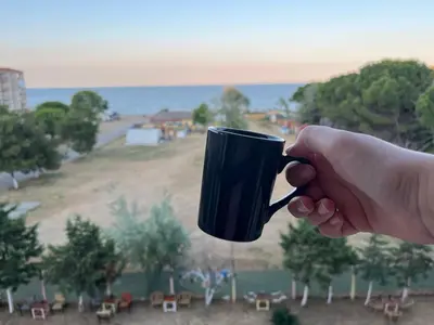 a hand holding a black coffee mug with a view of a field at Kumbağ Otel in Kumbağ