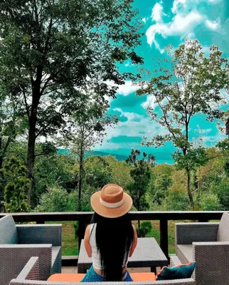 a woman in a hat sitting on a balcony looking out at the trees at Sapanca Balkaya Bungalov Dağ evi in Sapanca