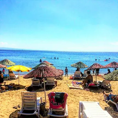 a beach with chairs and umbrellas and people in the water at Ceti̇n Presti̇ge Resort in Erdek