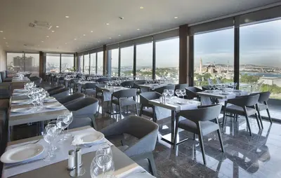 a restaurant with white tables and chairs and windows at Hotel Arcadia Blue Istanbul in Istanbul