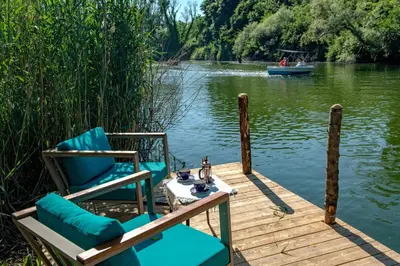 two chairs and a table on a dock with a boat at Wineport Lodge Agva Riverside Hotel & Winery in Agva