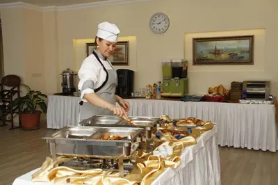 a woman preparing food on a table in a kitchen at Sahil Hotel Pendik in Tuzla