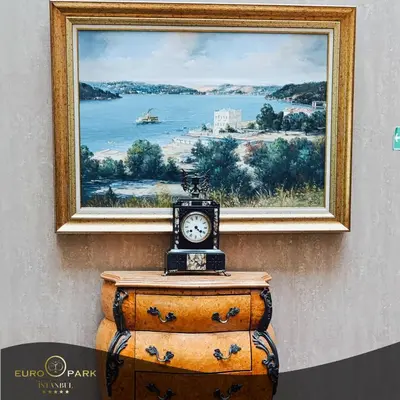 a clock on top of a dresser in front of a painting at Euro Park Otel in Istanbul