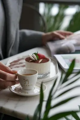 a person holding a cup of coffee next to a cake at 39 Kalamış Marina Hotel & Restaurant in Istanbul