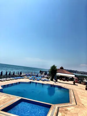 a swimming pool next to a beach with chairs and the ocean at Family Resort Hotel in Selimpasa