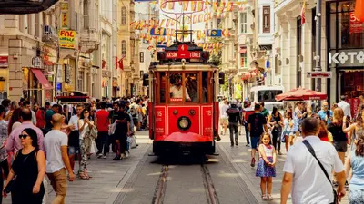 a red trolley car driving down a busy city street at Taksim Square Leon's Hotel in Istanbul